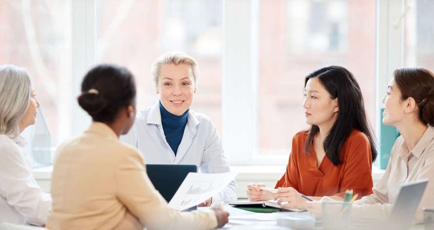 Portrait of diverse group of businesswomen discussing project while sitting at table during meeting in office, focus on smiling female boss